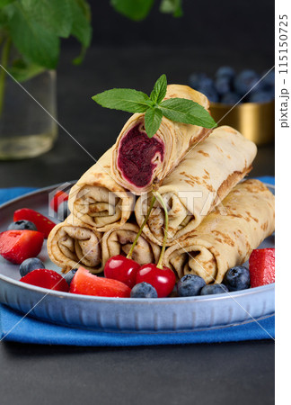 Crepes stacked in a pile, one of which is cut and filled with berry filling. The plate is also decorated with blueberries Crepes stacked in a pile, one of which is cut and filled with berry filling. The plate is also decorated with blueberries 115150725