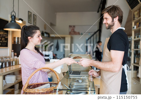 Handsome shop assistant serving customer in package-free store using reusable containers. Zero waste shops offering package-free bulk goods and sustainable alternatives. Handsome shop assistant serving customer in package-free store using reusable containers. Zero waste shops offering package-free bulk goods and sustainable alternatives. 115150755