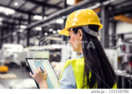 Female project manager standing in modern industrial factory. Manufacturing facility with robotics, robotic arms and automation. Storing products and materials in warehouse. 115150790