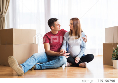 Beautiful young couple expecting a baby, moved into new home. Sitting among cardboard boxes. New beginnings. 115150796