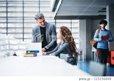 Handsome university professor helping female student with final project, showing her research paper, book for thesis in library. Handsome university professor helping female student with final project, showing her research paper, book for thesis in library. 115150849