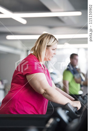 Overweight woman exercising on treadmill in gym. Overweight woman exercising on treadmill in gym. 115150902