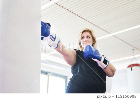 Overweight woman is working out in gym, boxing as part of her cardio training, wearing boxing gloves. Overweight woman is working out in gym, boxing as part of her cardio training, wearing boxing gloves. 115150908