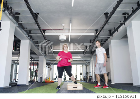 Overweight woman exercising in gym. Personal trainer couching her and helping her. 115150911
