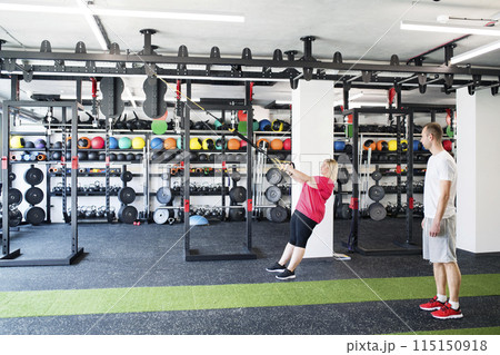 Overweight woman exercising in gym. Personal trainer couching her and helping her. 115150918