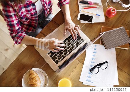 A beautiful university student is writing her thesis on a laptop, sitting at home on the couch. A beautiful university student is writing her thesis on a laptop, sitting at home on the couch. 115150935