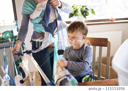 Young son helping mother with hosehold chores, hanging clothes on drying rack. Weekly chores, weekend activities. 115151056