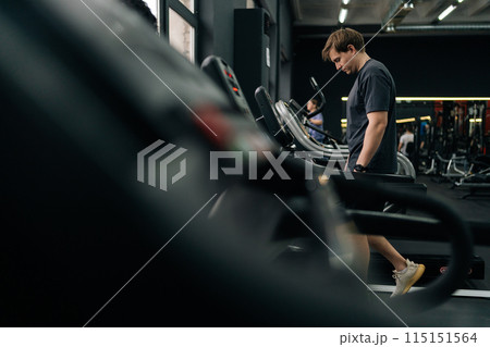Side view of tired athletic man walking on treadmill preforming warming-up run routine exercise in gym. Sporty male walking on running track, working on health and fitness. Concept of healthy life. Side view of tired athletic man walking on treadmill preforming warming-up run routine exercise in gym. Sporty male walking on running track, working on health and fitness. Concept of healthy life. 115151564