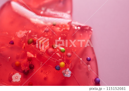 Colorful candy on a red background with water drops and bubbles. Colorful gel texture, clear skincare cream with bubbles and decorative figurines background, transparent beauty serum, colored cosmetic Colorful candy on a red background with water drops and bubbles. Colorful gel texture, clear skincare cream with bubbles and decorative figurines background, transparent beauty serum, colored cosmetic 115152081