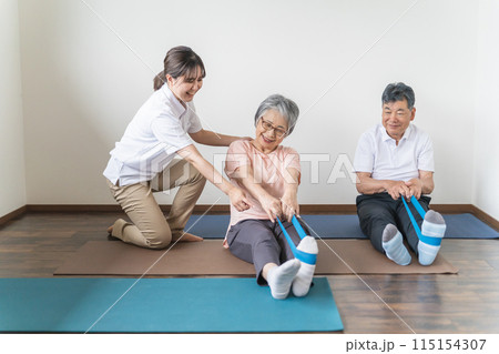 老人ホームでチューブトレーニング・リハビリするシニア・高齢者の男女と理学療法士・介護士・トレーナー 115154307