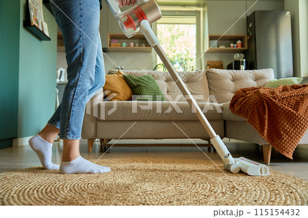 Woman is vacuuming floor of modern apartment living room with vacuum cleaner Woman is vacuuming floor of modern apartment living room with vacuum cleaner 115154432