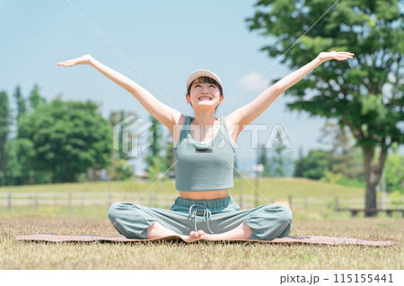 公園でヨガマットを使ってヨガ・ストレッチ・深呼吸・リフレッシュをする女性（晴れ・天気） 115155441