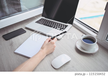 Unrecognizable woman hands writing in empty mock up notebook and computer. Freelancer using smart phone and laptop at home during quarantine. 115158432