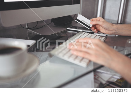 Unrecognized woman holding credit card in hand and using laptop computer keyboard. Online shopping, e-commerce, internet banking, spending money concept Unrecognized woman holding credit card in hand and using laptop computer keyboard. Online shopping, e-commerce, internet banking, spending money concept 115158573