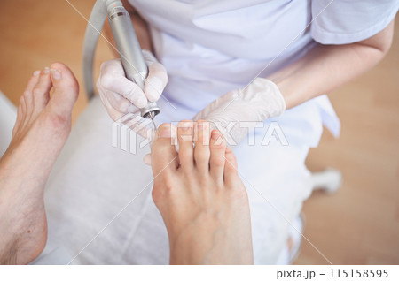 Hardware medical pedicure with nail file drill apparatus. Patient on pedicure treatment with pediatrician chiropodist. Foot peeling treatment at spa with a special device. Clinic of Podiatry Podology 115158595