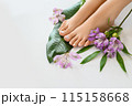Beautiful perfect female skin legs feet top view with tropical flowers and green palm leaf. Nail polish, care and clean, spa pedicure treatment in white. Concept on background isolated. Copy space 115158668