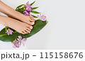 Beautiful perfect female skin legs feet top view with tropical flowers and green palm leaf. Nail polish, care and clean, spa pedicure treatment in white. Concept on background isolated. Copy space 115158676