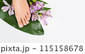 Beautiful perfect female skin legs feet top view with tropical flowers and green palm leaf. Nail polish, care and clean, spa pedicure treatment in white. Concept on background isolated. Copy space 115158678