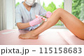 Woman with long tanned perfect legs and smooth skin having wax stripe depilation hair removal procedure on legs in beauty salon. Beautician in blue robe, pink gloves. Body care, epilation spa concept 115158683