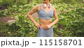 Young unrecognizable beautiful slim fit girl in blue sportswear with big white headphones doing sports and fitness in the summer park outside. Girl with perfect body doing yoga or exercises 115158701