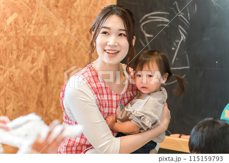 園児の女の子を抱っこする笑顔の保育士・保母さん・ベビーシッターの若いアジア人女性 115159793