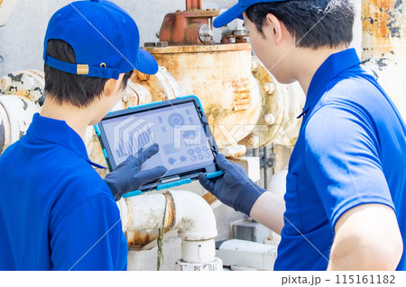 タブレットを見ながら配管・機械を点検するエンジニアのグループ 115161182