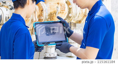 タブレットを見ながら配管・機械を点検するエンジニアのグループ 115161184