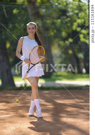 A woman is holding a tennis racket and standing on a tennis court 115161694
