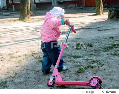 Little girl and her scooter. Little girl to drive a scooter to teach yourself Little girl and her scooter. Little girl to drive a scooter to teach yourself 115162900