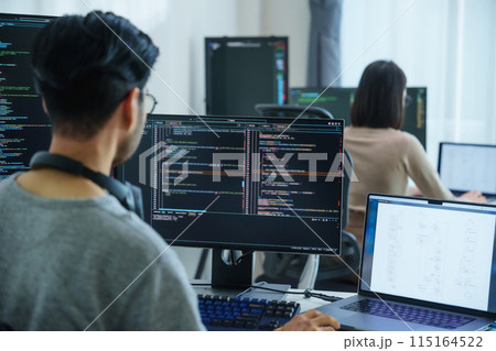 Asian software developers working on multiple screens displaying code and application diagrams in a modern office 115164522