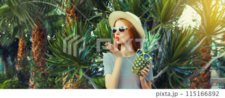 Summer portrait of beautiful young woman with pineapple fruits posing blowing a kiss, palm trees Summer portrait of beautiful young woman with pineapple fruits posing blowing a kiss, palm trees 115166892