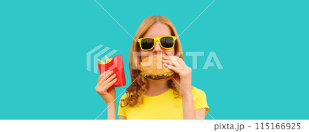 Portrait of happy cheerful young woman eating burger fast food and french fries, fried potatoes 115166925