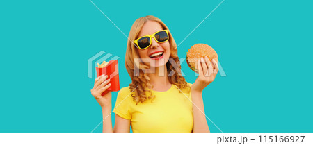 Portrait of happy cheerful young woman eating burger fast food and french fries, fried potatoes Portrait of happy cheerful young woman eating burger fast food and french fries, fried potatoes 115166927