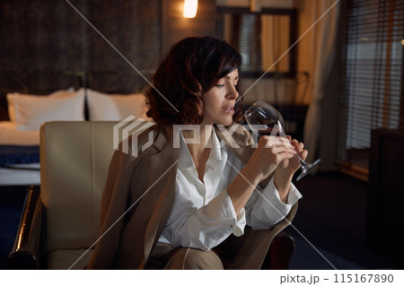 Thoughtful businesswoman drinking wine in luxurious hotel room Thoughtful businesswoman drinking wine in luxurious hotel room 115167890
