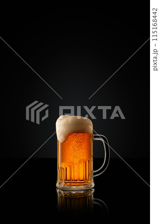 Glass mug of cold, refreshing, golden beer, topped with thick foam against black studio background. 115168442