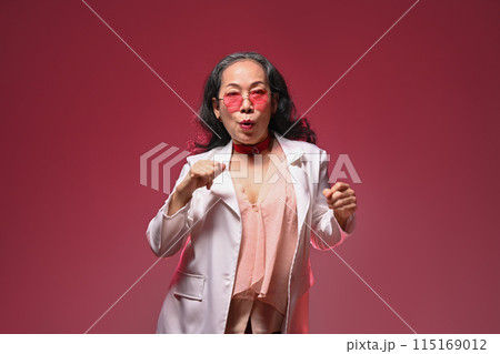 Happy and carefree middle age woman with sunglasses dancing over red background 115169012