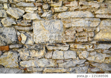 Stones of different sizes textures and varying degrees of destruction are chaotically fixed in the wall Stones of different sizes textures and varying degrees of destruction are chaotically fixed in the wall 115169506
