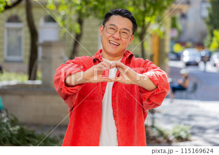 Asian man makes symbol of love, showing heart sign to camera, express romantic positive feelings Asian man makes symbol of love, showing heart sign to camera, express romantic positive feelings 115169624