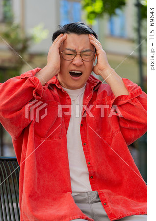 Sad unhappy frustrated Asian man sitting alone in city street, feeling bad, annoyed, grief, problem 115169643
