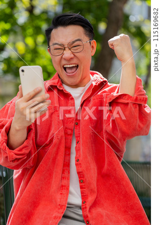 Asian man use mobile smartphone celebrating win good message news outdoors on urban city street 115169682