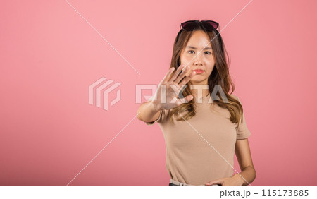 Asian beautiful woman itching her outstretched hand showing stop gesture front face on pink background with copy space, female doing show stop sign with palm of hand Asian beautiful woman itching her outstretched hand showing stop gesture front face on pink background with copy space, female doing show stop sign with palm of hand 115173885