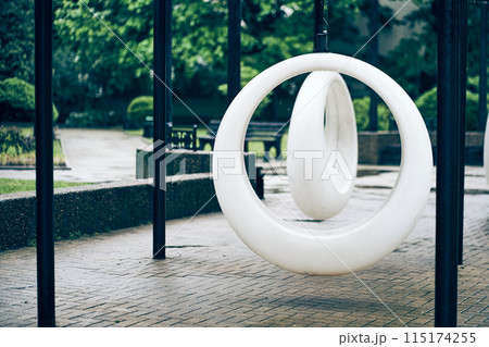 Recreation area in the park. Rocking benches in the park in summer. With space to copy. A park with white round swings in cloudy weather. High quality photo 115174255