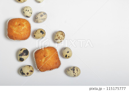 Quail eggs lie on the white surface. Nearby are cupcakes.  Next to the box with a gift wrapped in wrapping paper and tied with a ribbon. 115175777