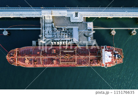 Aerial top down view of a large oil tanker docked at a pier in the port in process of loading. Aerial top down view of a large oil tanker docked at a pier in the port in process of loading. 115176635
