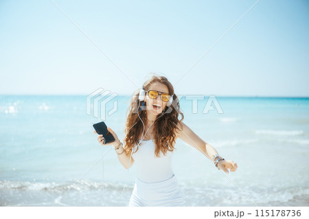 smiling woman on ocean shore dancing and listening to music 115178736