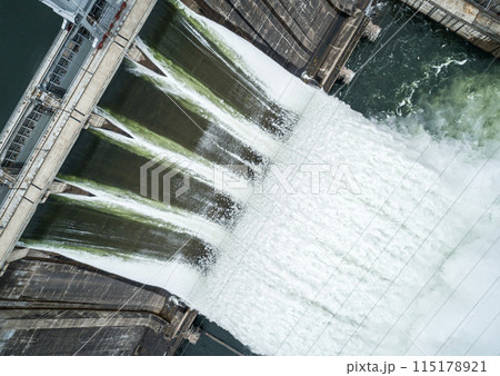 Aerial top down view of concrete dam releasing water into river on cloudy day. Water discharge at hydroelectric power plant. 115178921