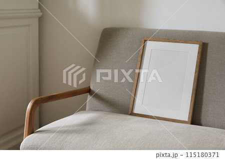 Closeup of blank wooden picture frame, poster mockup, midcentury linen sofa in sunlight. White wall background. Elegant minimal Scandinavian interior. Art display. Home decor concept. Cozy still life. Closeup of blank wooden picture frame, poster mockup, midcentury linen sofa in sunlight. White wall background. Elegant minimal Scandinavian interior. Art display. Home decor concept. Cozy still life. 115180371