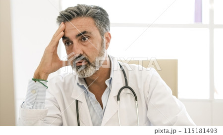 Tensed bearded male doctor with head in hand in clinic 115181493