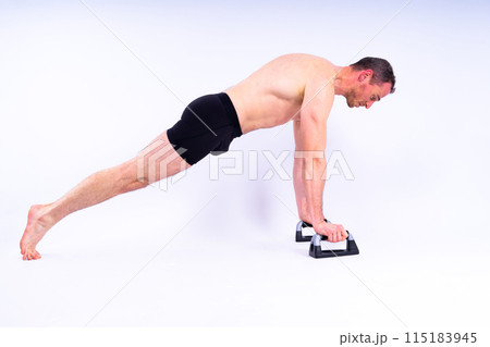 Shirtless muscular athlete doing push-up on push up bars. Full body man on white studio background. 115183945