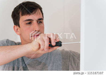 Close-up of a young professional carpenter using a hand-held screwdriver 115187107